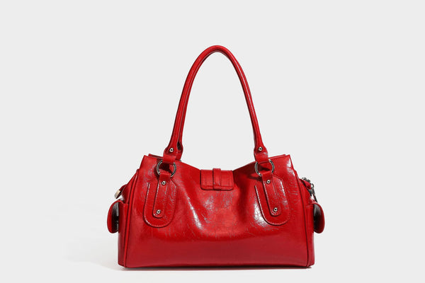 Glänzende, geknautschte Barrel-Satchel mit zwei oberen Tragegriffen, vorderem Klappen-Riemen-Panel, Ring- und Nietenbeschlägen sowie einem abnehmbaren
