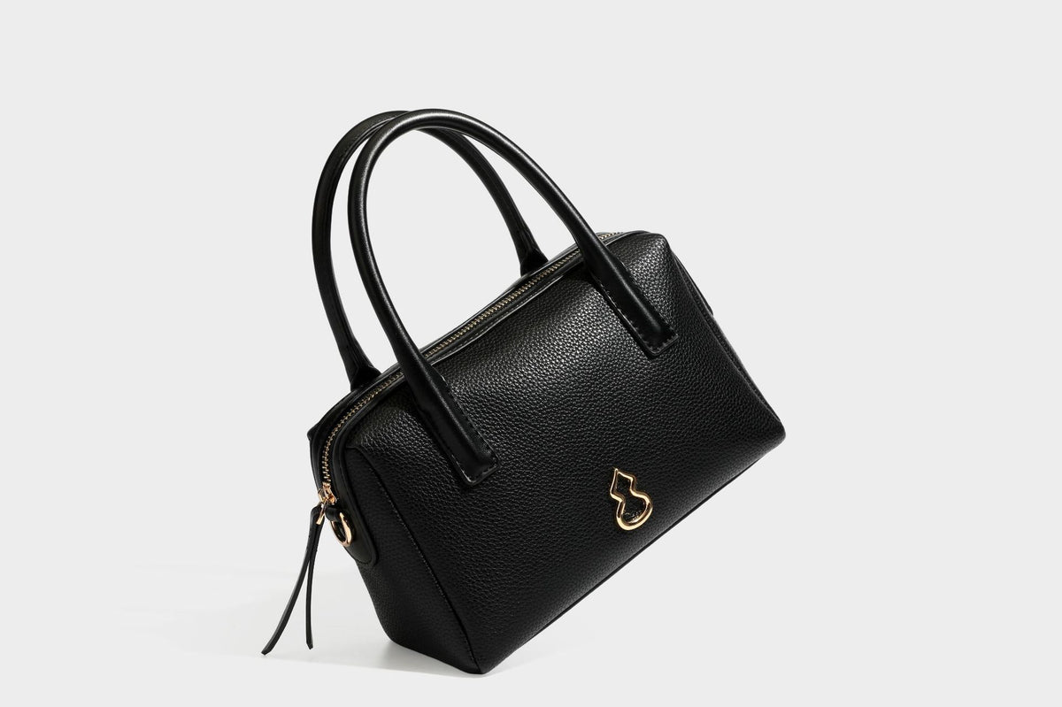 Small structured pillow satchel bag with pebbled leather-look finish, dual rolled top handles, gold-tone gourd emblem, and