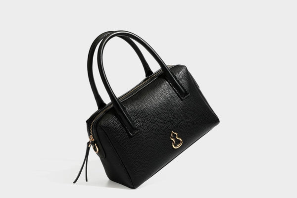 Small structured pillow satchel bag with pebbled leather-look finish, dual rolled top handles, gold-tone gourd emblem, and