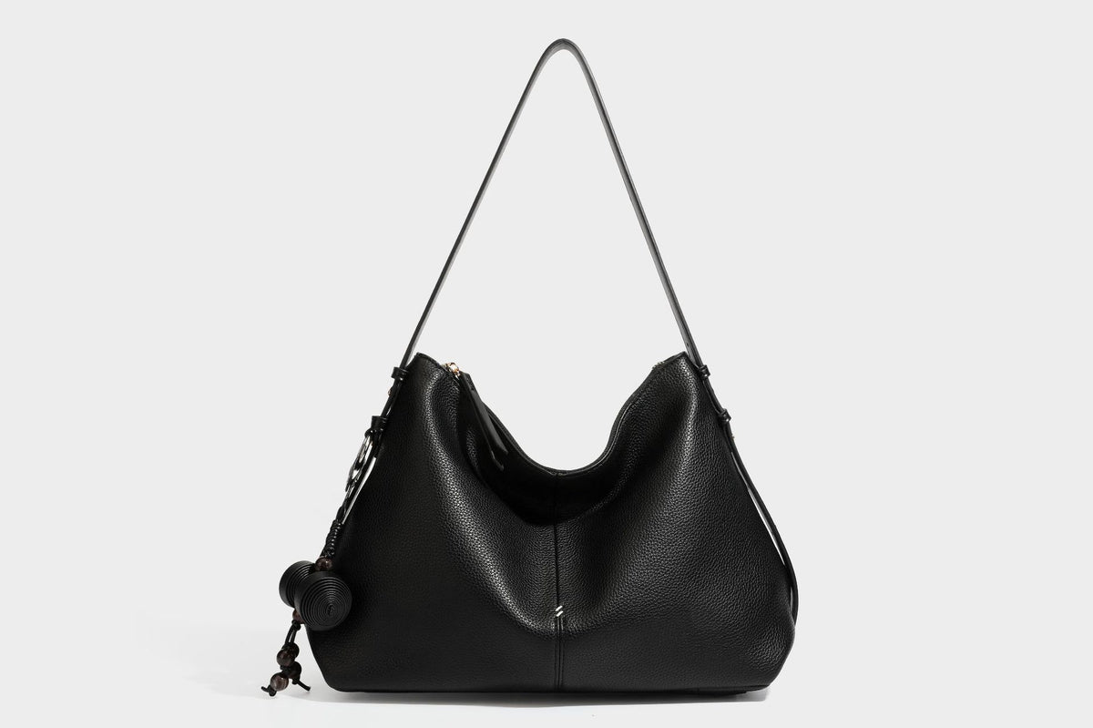 Slouchy hobo shoulder bag with pebbled leather-look finish, zip-top closure, gold-tone hardware, and hanging bead charm