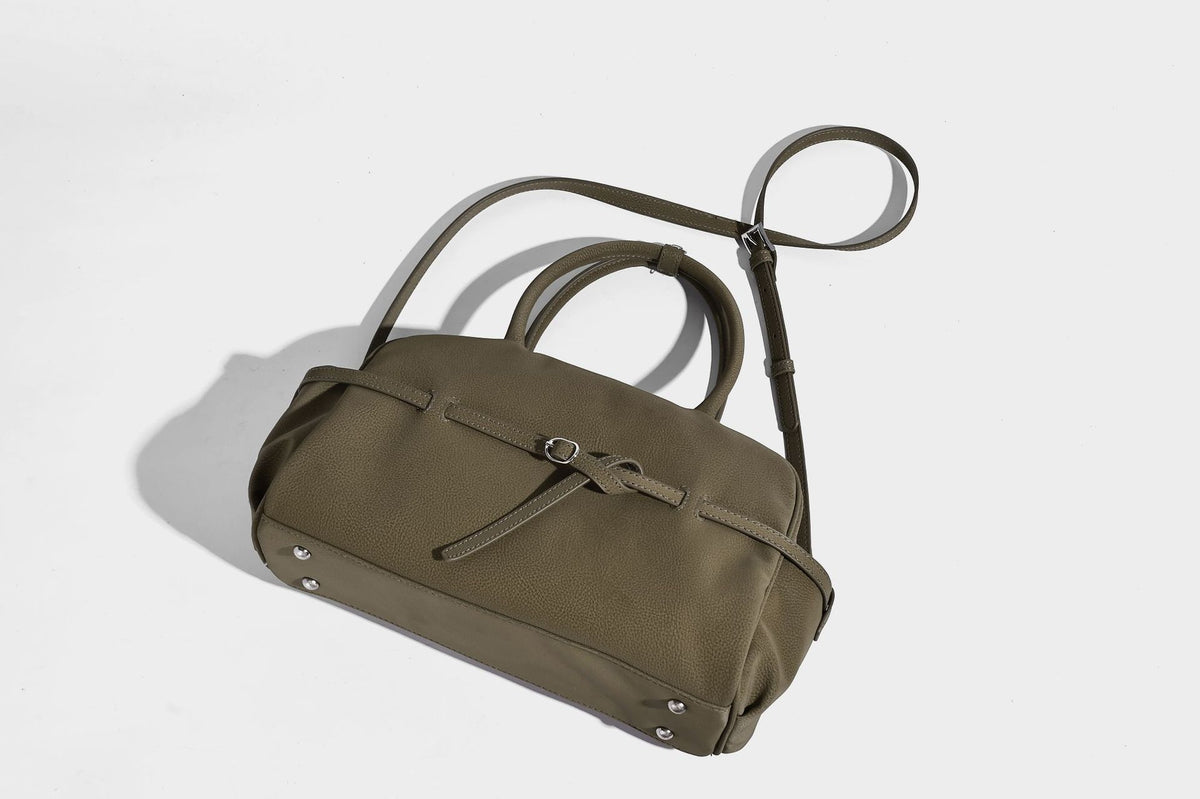 Strukturierte Henkeltasche aus mattem, genarbtem Material mit umlaufendem Riemen und Ringbeschlägen, zwei oberen Tragegriffen und abnehmbarem Crossbody-Riemen