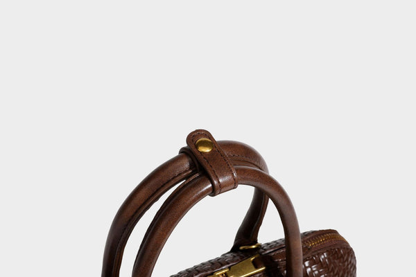 Structured woven-embossed leather-look satchel with dual rolled top handles, gold-tone turn-lock closure, and detachable
