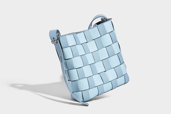 Hand-woven black-and-white checkerboard bucket bag with smooth black trim, silver-tone ring hardware, and adjustable