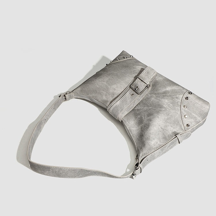 Slouchy trapezoid hobo shoulder bag with distressed textured finish, silver rivet corner accents, centre buckle strap, and