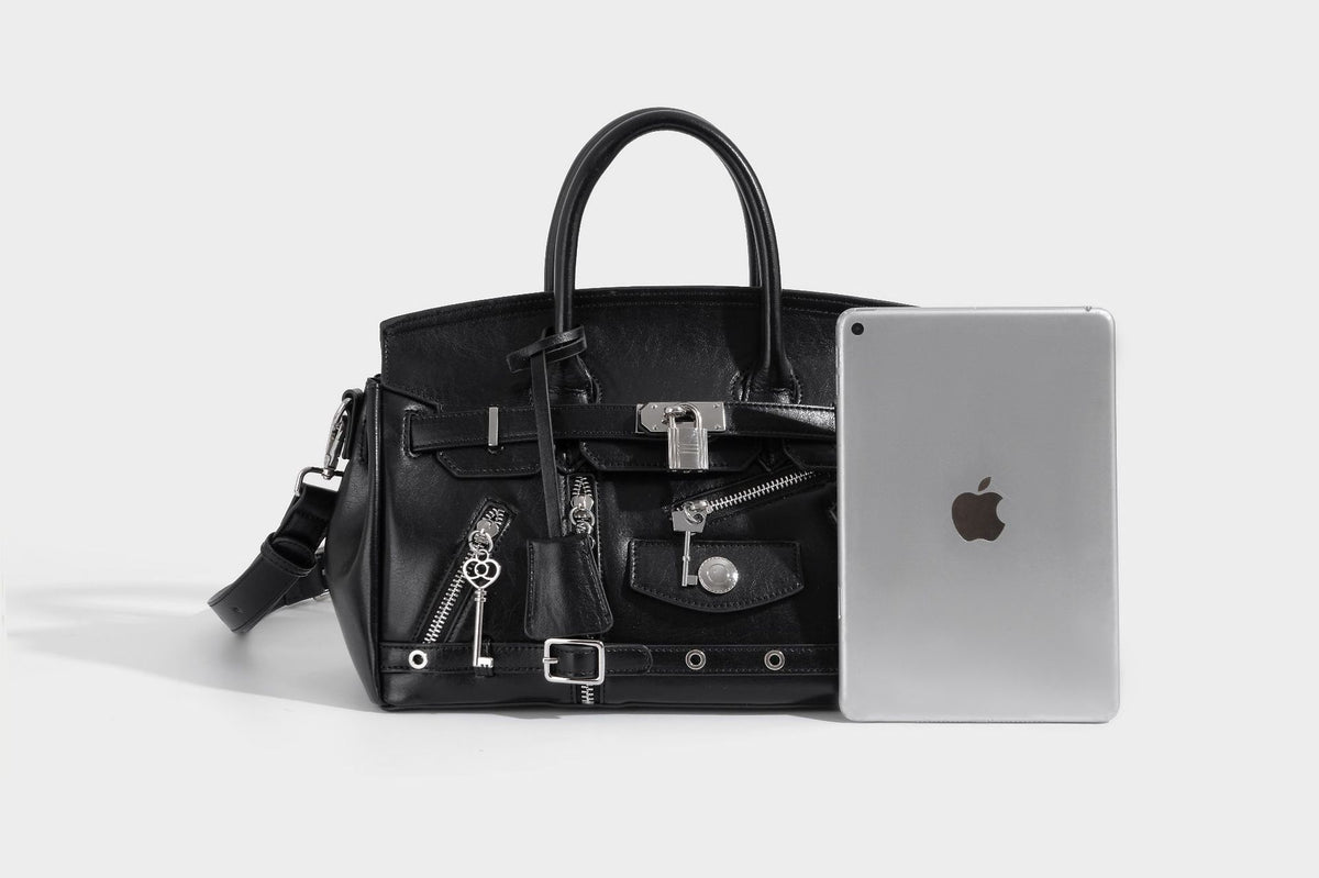 Structured black leather-look satchel bag with silver padlock hardware, front zip pockets, key charms, and top handles