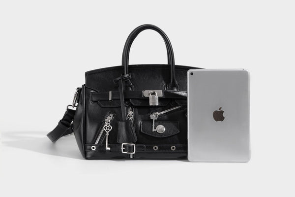 Structured black leather-look satchel bag with silver padlock hardware, front zip pockets, key charms, and top handles