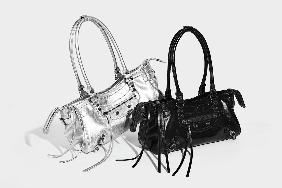 Längliche Schultertasche in Zylinderform mit glänzender Lederoptik, silberfarbenen Nietenbeschlägen, seitlichen Quasten und mehreren außenliegenden Reißverschlüssen