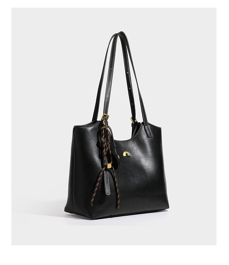 Structured smooth leather-look tote bag with long shoulder strap, gold-tone hardware, and hanging tassel-coin charm, detail