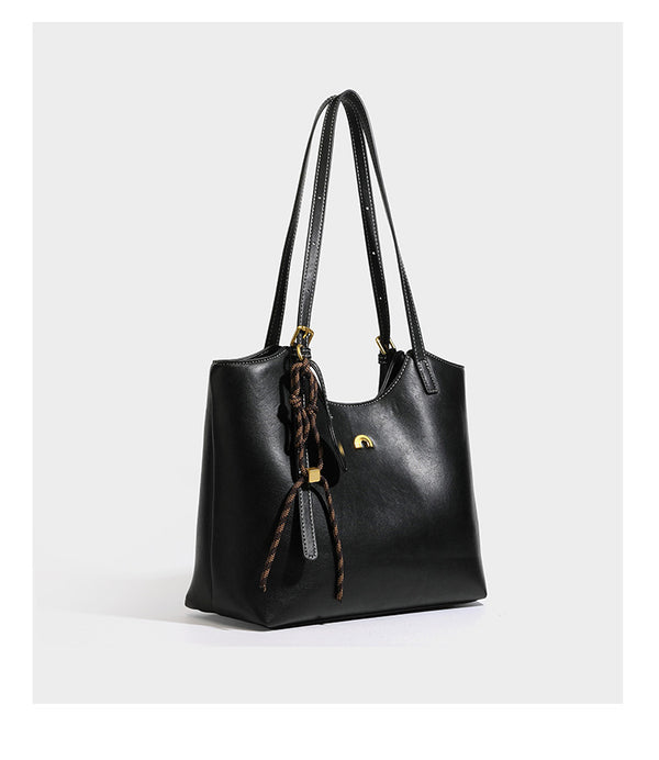 Structured smooth leather-look tote bag with long shoulder strap, gold-tone hardware, and hanging tassel-coin charm, detail