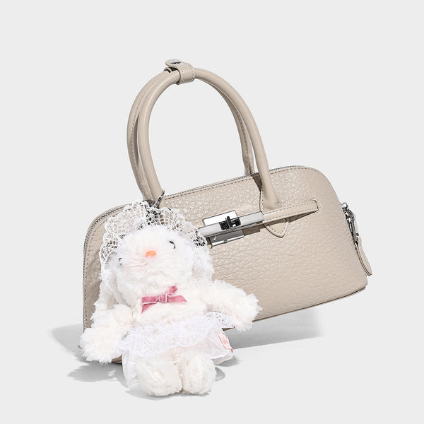 Small structured shell-silhouette top-handle bag with pebbled leather-look finish, silver-tone turn-lock hardware, and