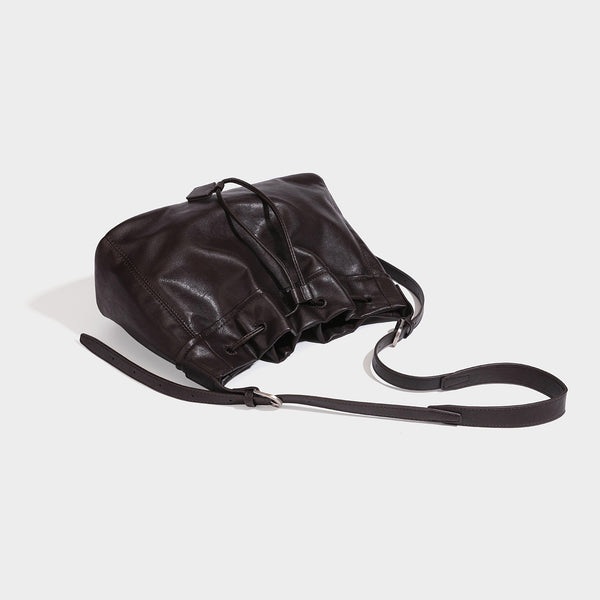 Slouchy drawstring bucket bag in dark brown leather-look finish with long adjustable shoulder strap and gathered tie closure
