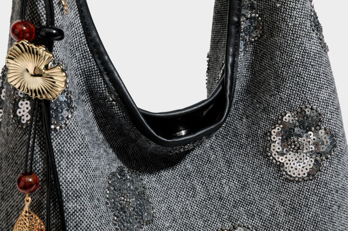 Lässig fallende, trapezförmige Schulter-Tote in Anthrazitgrau mit floralen Paillettenmotiven in Silber, Riemen in Lederoptik und herabhängendem Perlenbesatz