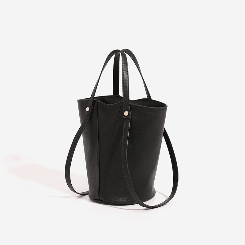 Structured black leather-look bucket tote bag with slim shoulder straps, silver-tone stud hardware, and tapered body, detail