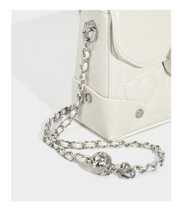 Kleine strukturierte Box-Tasche aus herzförmig gestepptem PU mit Henkel, silberfarbenem Kettenriemen zum Tragen als Crossbody und ovalem Drehverschluss, Detailansicht