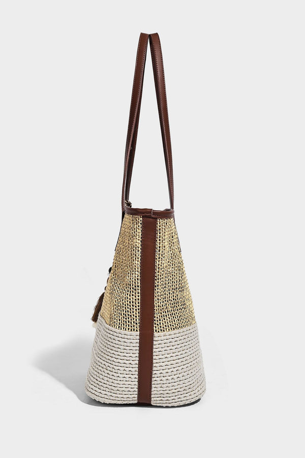 Woven straw-look tote bag in tan and cream with dark brown leather-look trim, long flat shoulder straps, and tassel bead
