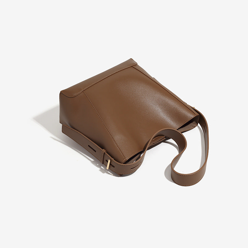 Structured smooth leather-look bucket shoulder bag with long adjustable strap and gold-tone buckle hardware in brown, detail