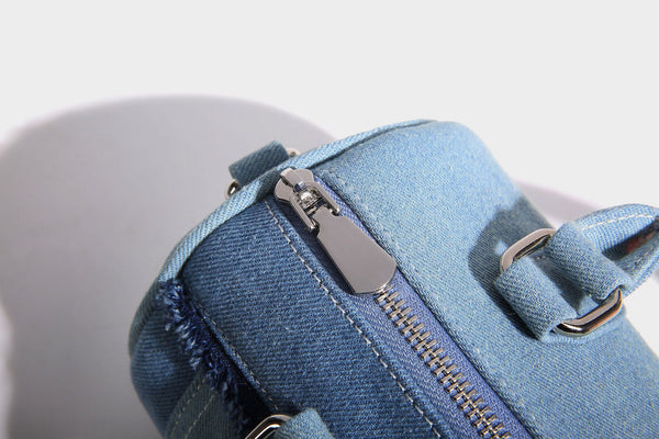 Mini barrel handbag in light and dark denim patchwork with frayed seam trim, dual top handles, top zip closure, and, detail