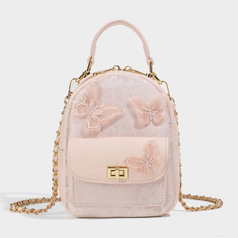 Structured mini backpack handbag with butterfly embroidery, gold-tone chain strap, and turn-lock front flap pocket, detail