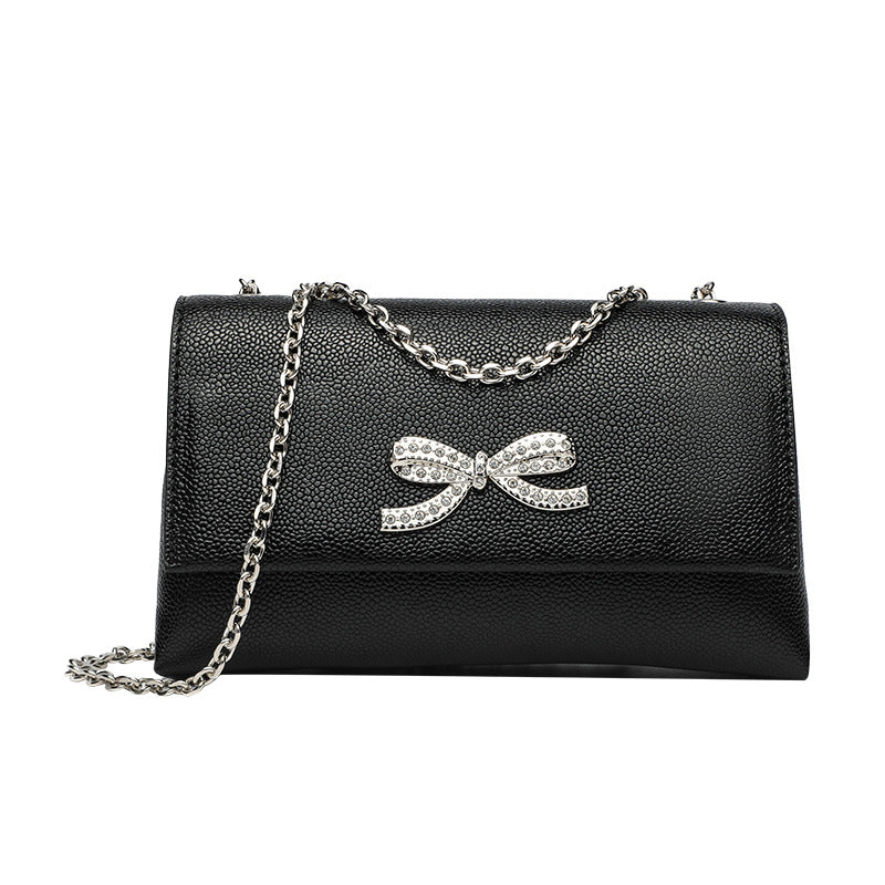 Structured rectangular flap crossbody bag with rhinestone bow and silver chain strap in pebbled finish, detail view 5