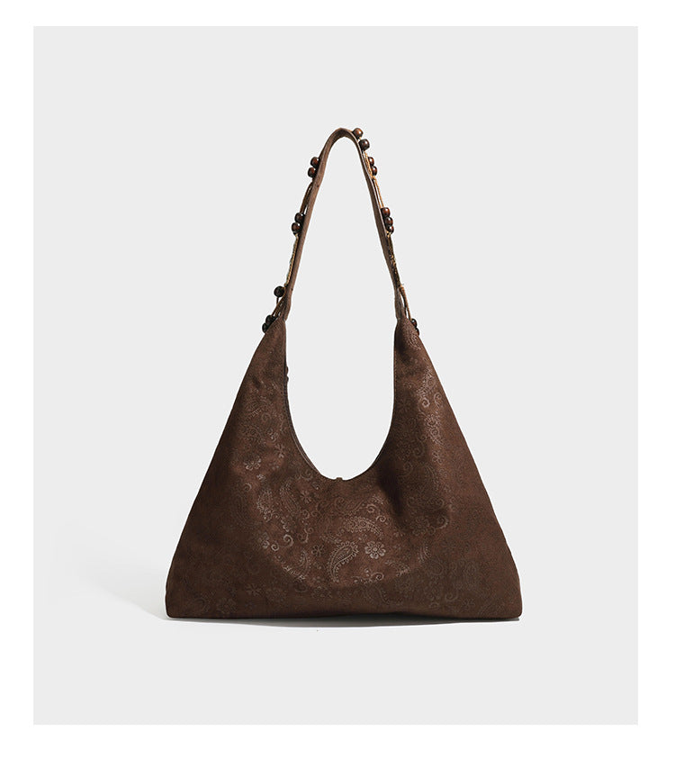 Slouchy boho hobo shoulder bag in embossed brown suede-look finish with beaded strap, cord tassels, and brass-tone leaf