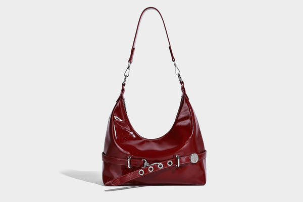 Glossy black slouchy hobo shoulder bag with silver-tone hardware, belt-style grommet strap at base, and long adjustable