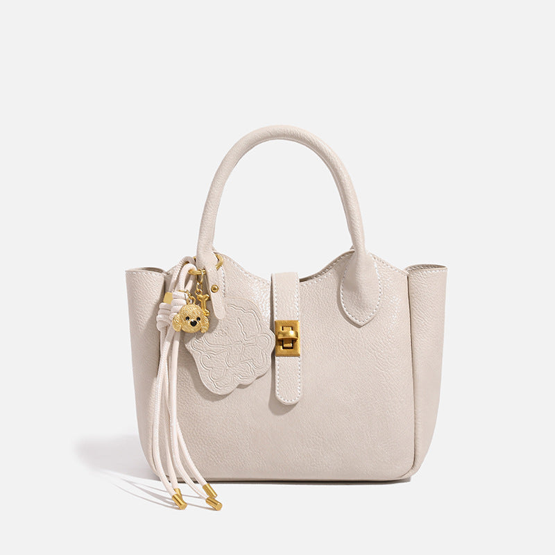 Small structured pebbled leather-look mini tote bag with gold-tone hardware, front toggle closure, knotted bear tassel charm