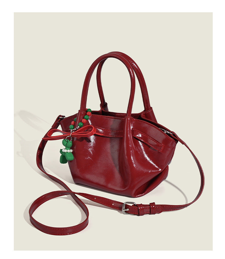Small structured red glossy PU handbag with bow-and-bead charm, dual top handles, and detachable crossbody strap, detail view