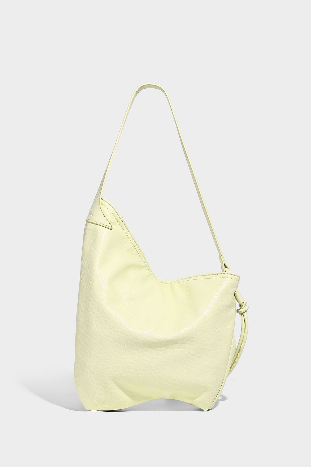 Slouchy hobo shoulder bag in pale yellow with slim strap, drawstring bead closure, and pink tulip floral charm, detail view