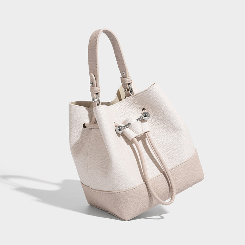 Small two-tone pebbled drawstring bucket bag with tan contrast base, metal toggle hardware, short top handle, and detachable