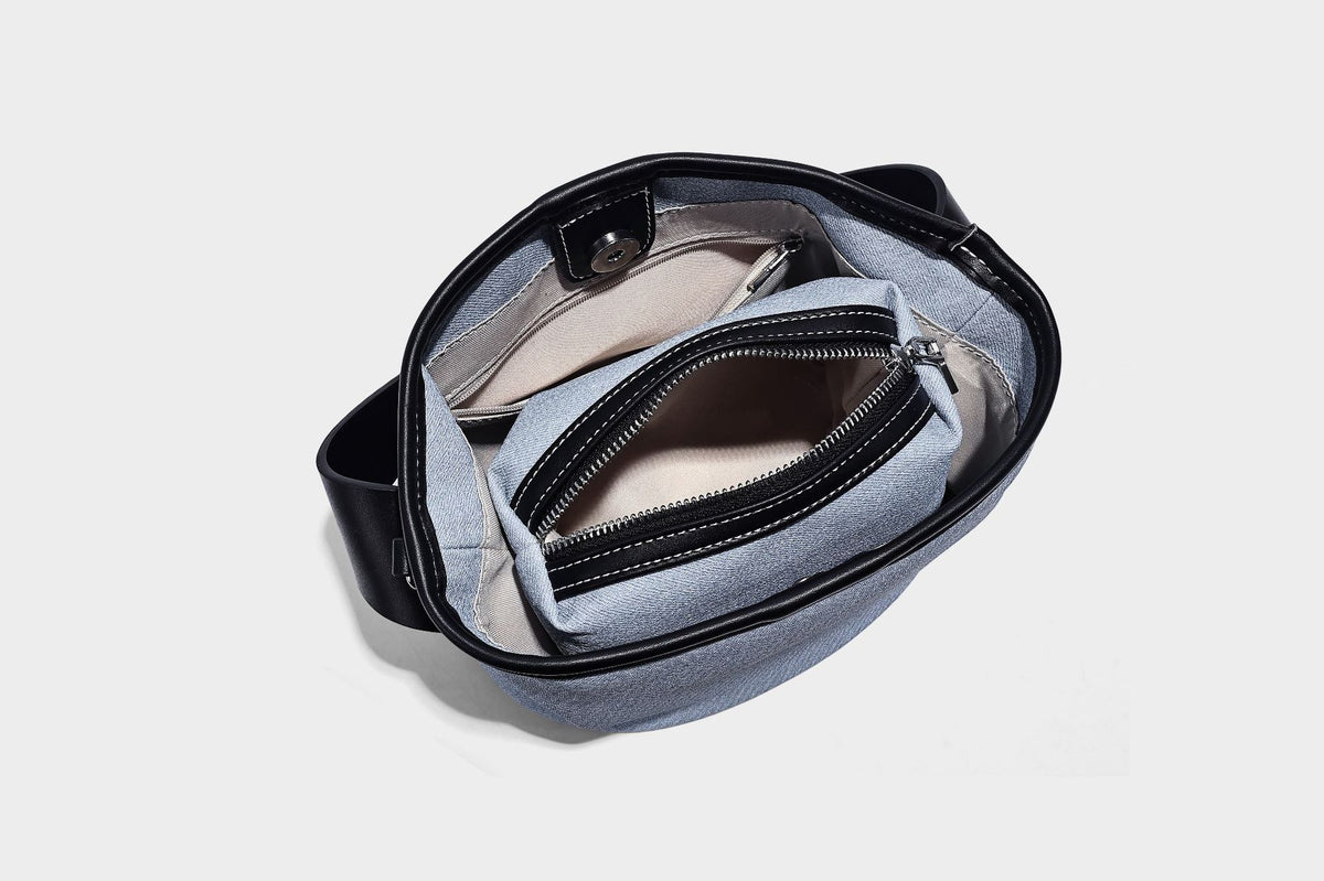 Hellblaue Bucket-Bag aus Denim mit schwarzem Besatz in Lederoptik, silberfarbenen Beschlägen, kurzem Tragegriff und langem verstellbarem Crossbody-Riemen