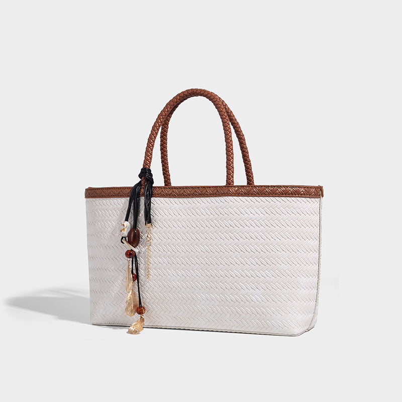 Structured woven-texture tote bag with brown braided top handles, decorative tassel charm, and detachable shoulder strap