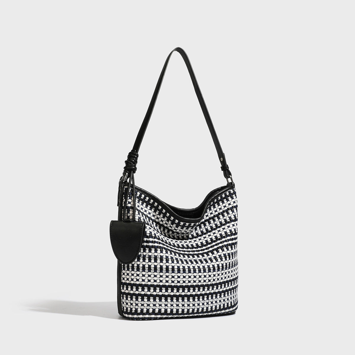 Woven stripe bucket shoulder bag in cream and dark brown with leather-look trim, knotted adjustable strap, and small shield