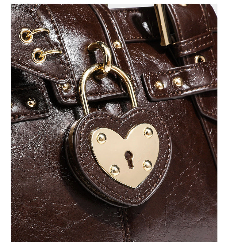 Structured leather-look satchel bag with heart padlock charm, star charm, gold-tone buckle hardware, dual top handles, and