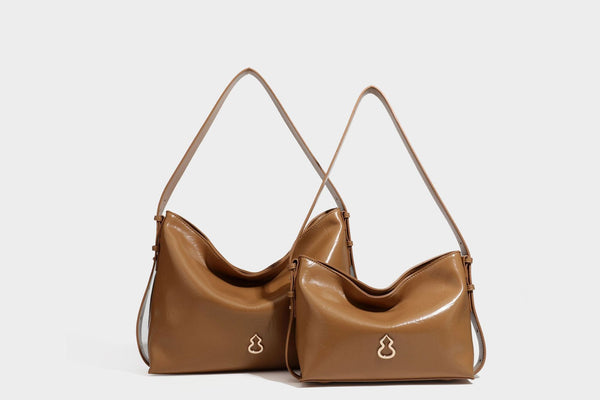 Lässig fallende Hobo-Schultertasche mit offenem Oberteil aus glänzender, karamellbrauner Lederoptik, mit Logo-Beschlägen in Goldoptik und langem, verstellbarem