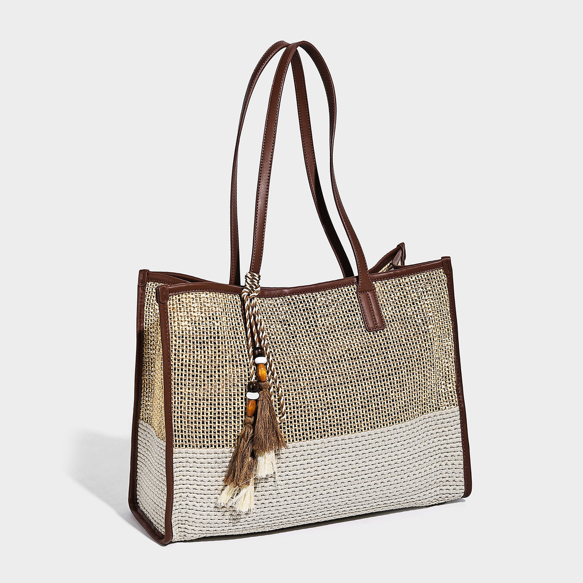Two-tone woven straw tote bag with leather-look brown trim, long shoulder straps, and knotted tassel charm, detail view 3