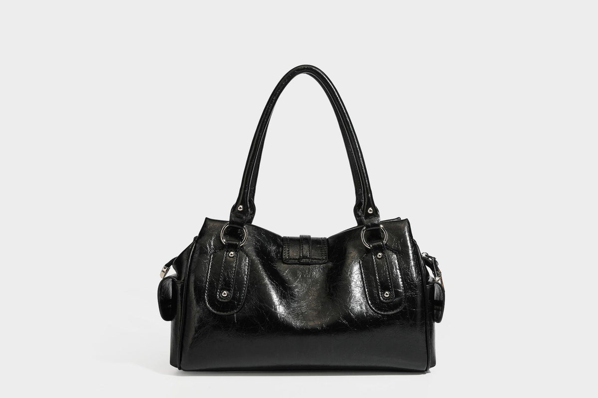 Glänzende, geknautschte Barrel-Satchel mit zwei oberen Tragegriffen, vorderem Klappen-Riemen-Panel, Ring- und Nietenbeschlägen sowie einem abnehmbaren