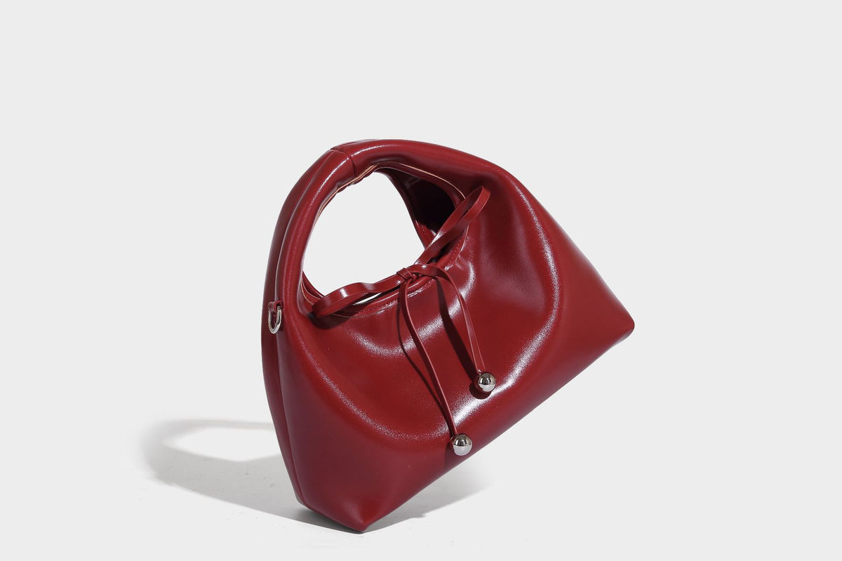 Kleine kuppelförmige Henkeltasche in glänzender Lederoptik mit Kordelzugverschluss, weißem Spitzen-Schleifenanhänger und silberfarbenen Metallbeschlägen