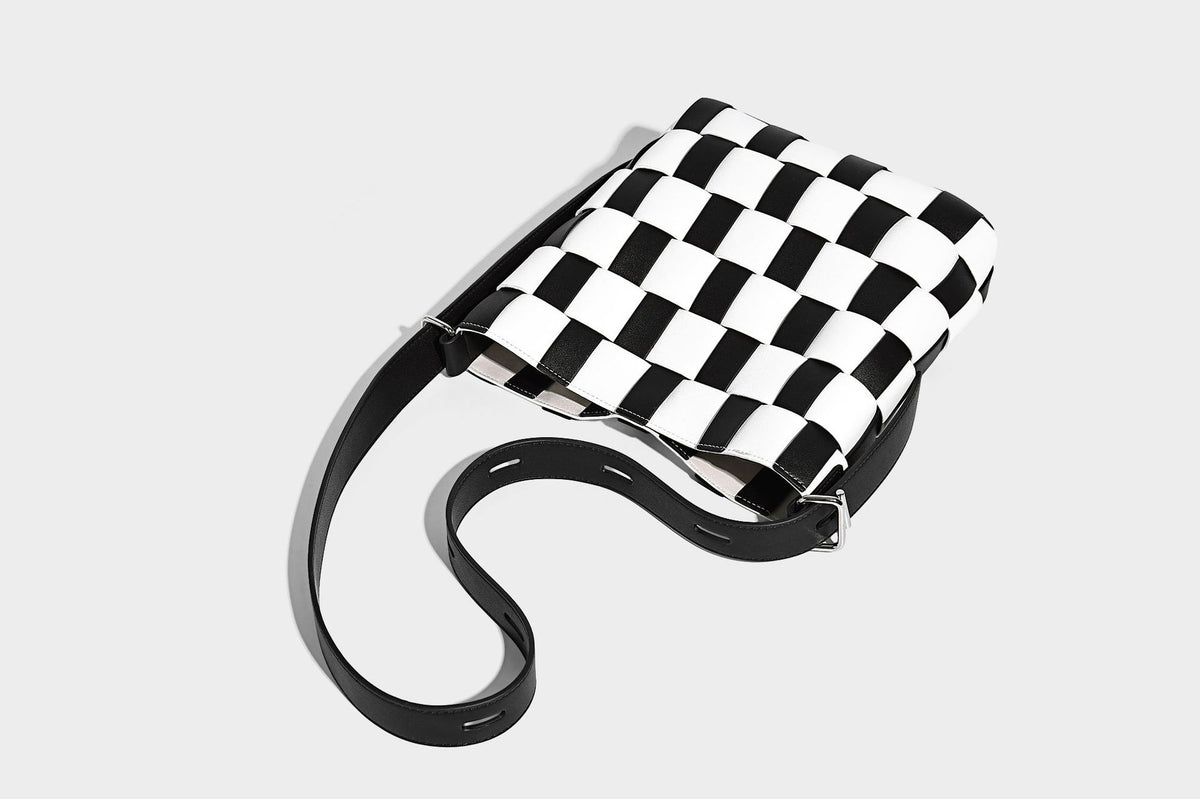 Hand-woven black-and-white checkerboard bucket bag with smooth black trim, silver-tone ring hardware, and adjustable