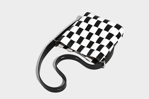 Hand-woven black-and-white checkerboard bucket bag with smooth black trim, silver-tone ring hardware, and adjustable