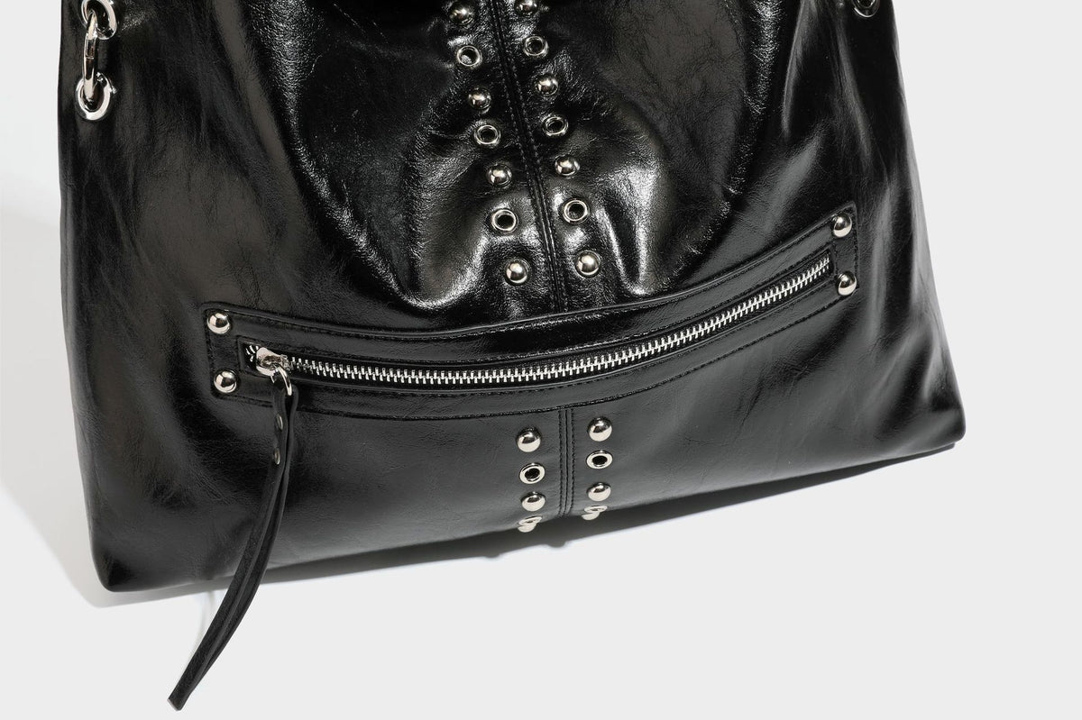 Black glossy leather-look slouchy shoulder bag with silver stud and eyelet hardware, top zip closure, front zip pocket, and