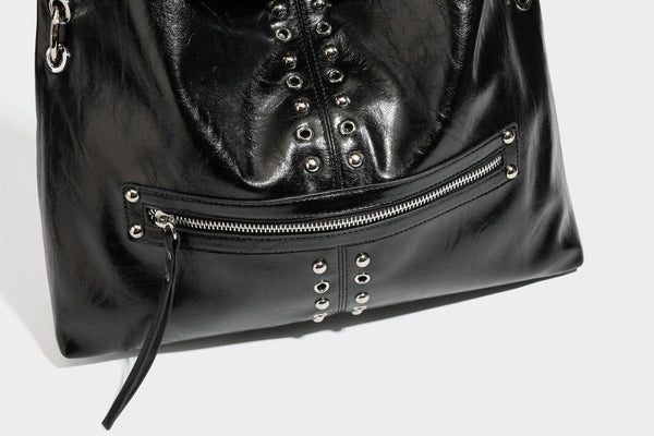 Black glossy leather-look slouchy shoulder bag with silver stud and eyelet hardware, top zip closure, front zip pocket, and