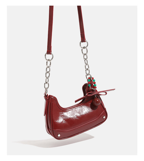 Small glossy cherry red crescent shoulder bag with silver chain strap, bead and tassel charm, and round pendant, detail view