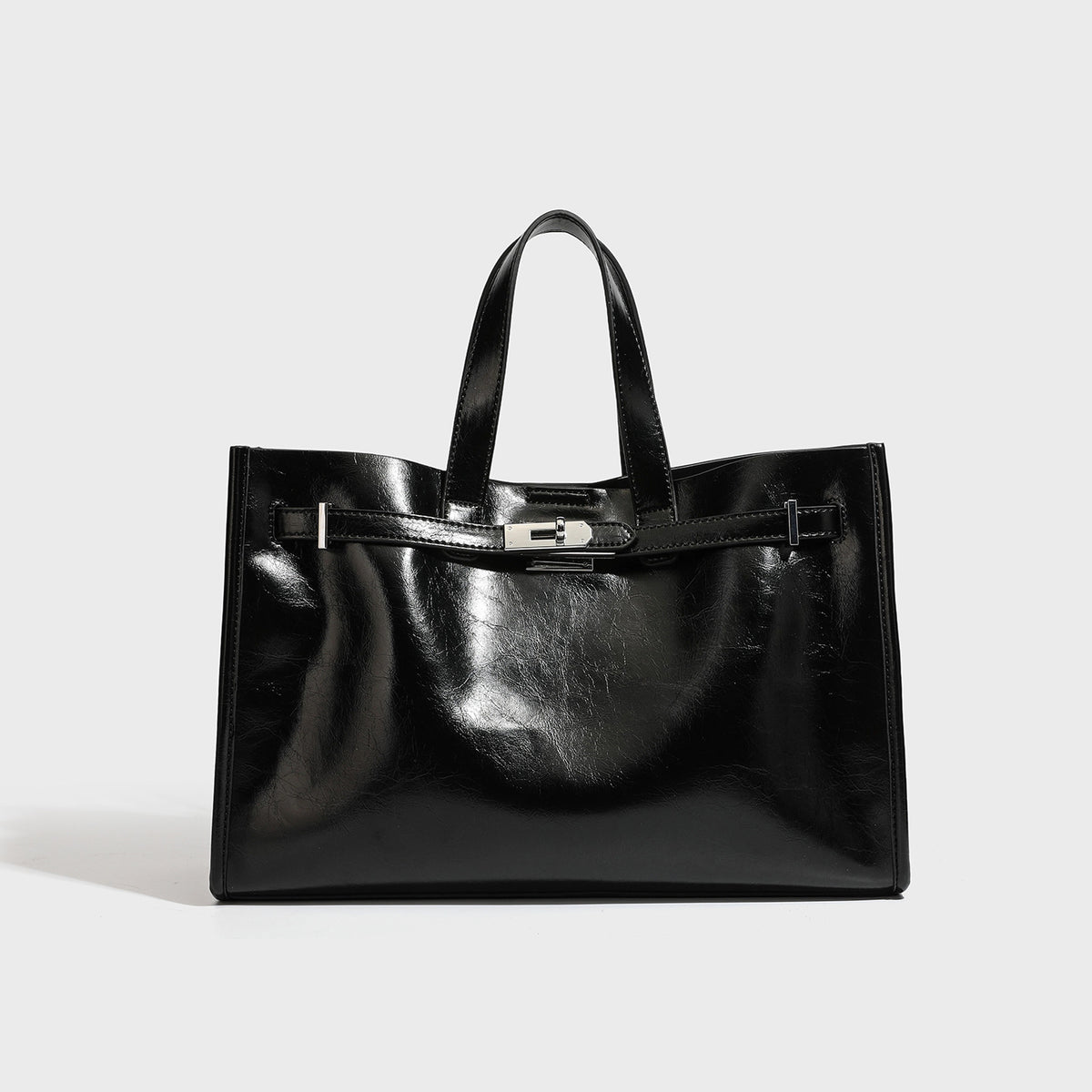 Strukturierte Tote-Bag in glänzender schwarzer Lederoptik mit Drehverschluss vorne, zwei Tragegriffen und abnehmbarem Schulterriemen