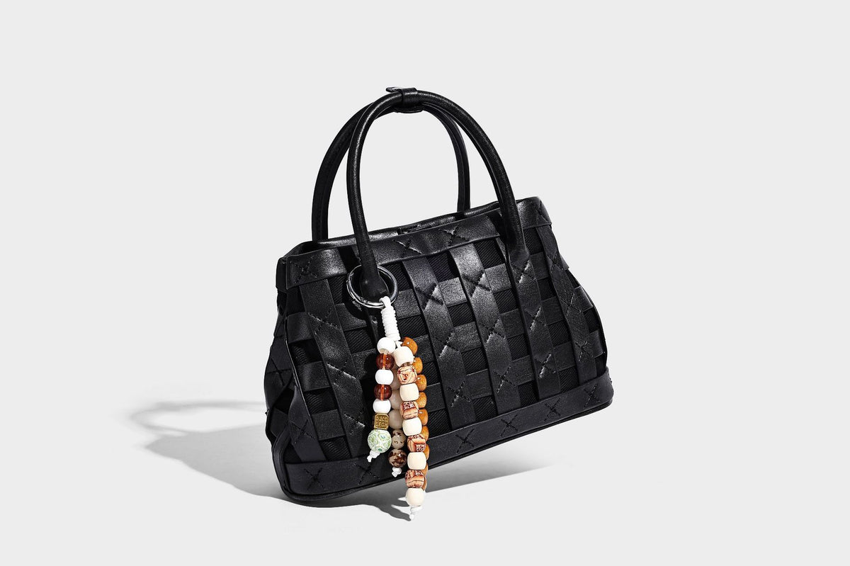 Small structured woven satchel tote with rounded top handles, silver-tone ring hardware, and bead tassel charm, detail view