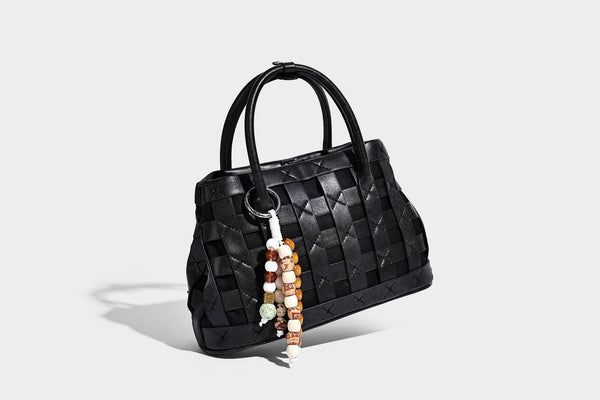 Small structured woven satchel tote with rounded top handles, silver-tone ring hardware, and bead tassel charm, detail view