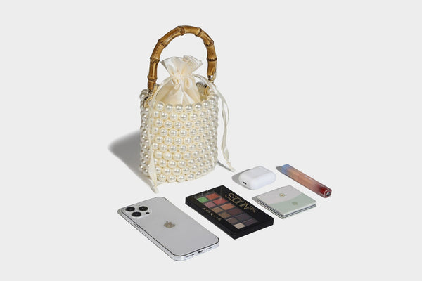 Small cylindrical bucket bag with glossy faux-pearl bead exterior, bamboo arched top handle, satin drawstring closure, and