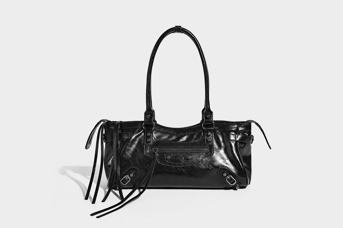 Längliche Schultertasche in Zylinderform mit glänzender Lederoptik, silberfarbenen Nietenbeschlägen, seitlichen Quasten und mehreren außenliegenden Reißverschlüssen