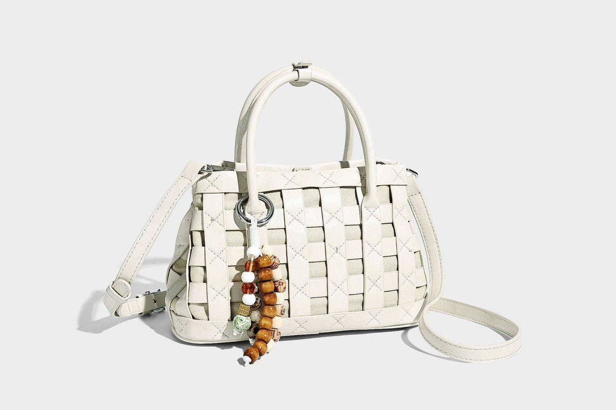 Small structured woven satchel tote with rounded top handles, silver-tone ring hardware, and bead tassel charm, detail view