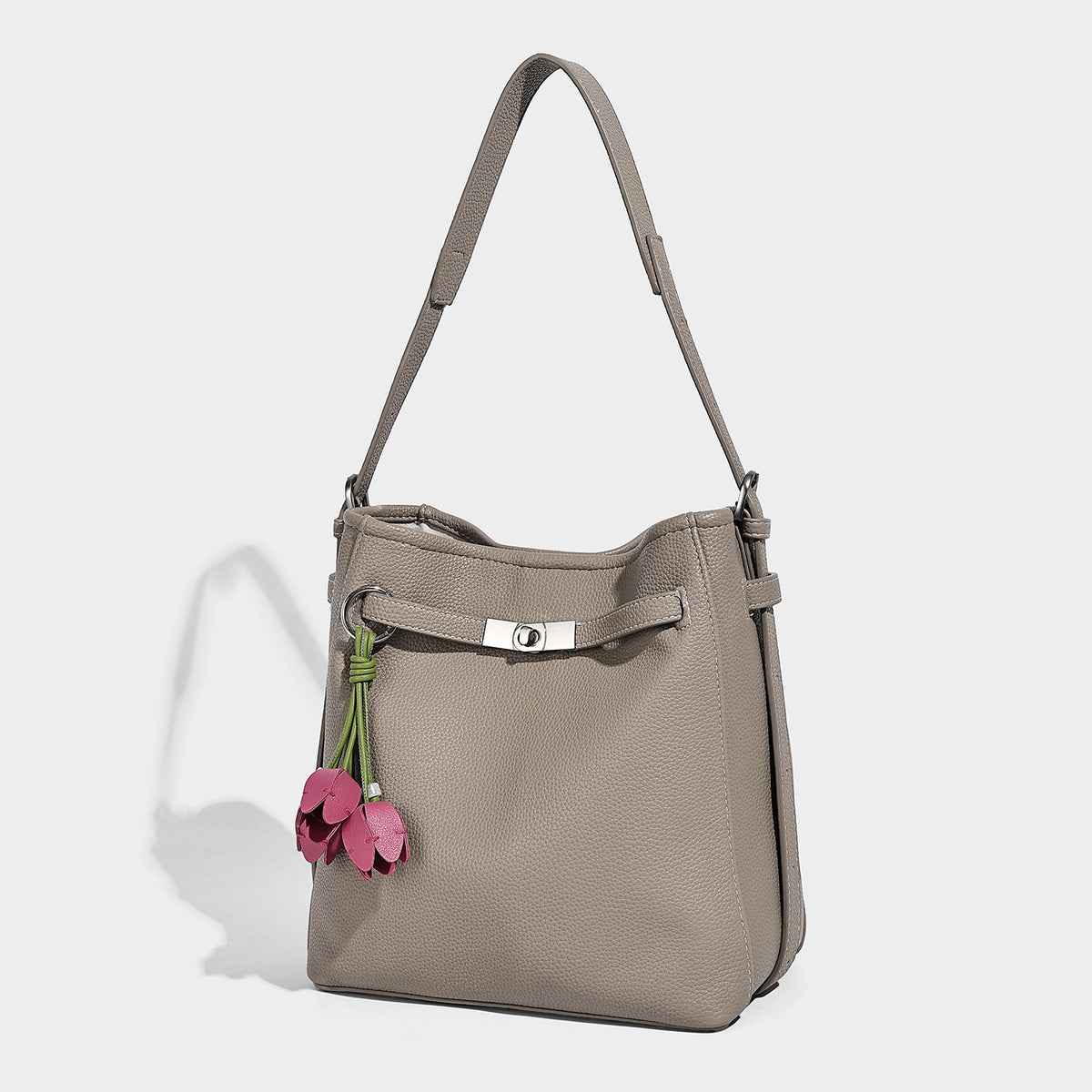 Soft-structured pebbled bucket shoulder bag with front turn-lock strap detail, adjustable strap, and hanging floral tassel