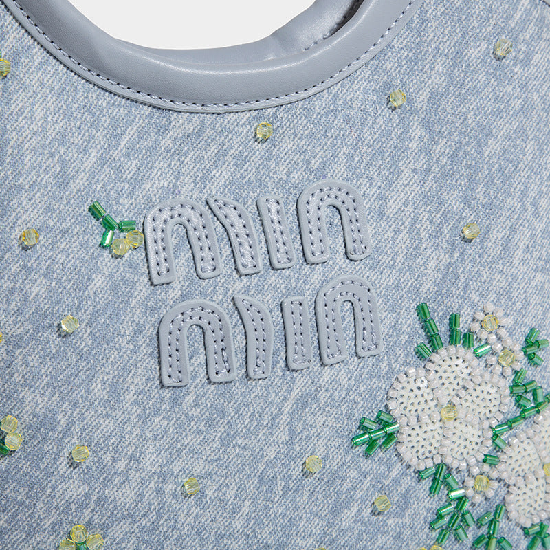 Kleine hellblaue Mini-Tote-Bag aus Stoff mit weißer Blumenverzierung aus Perlen, runden Tragegriffen, silberfarbenen Metallelementen und